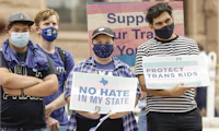 People standing together, holding signs with transgender flags and affirmative language at a rally