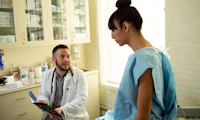 A transgender woman in a hospital gown speaking to her doctor a transgender man in an exam room
