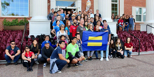 A large group of people standing in front of a building holding an HRC flag