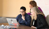 Group of coworkers crowded around a laptop on a table.