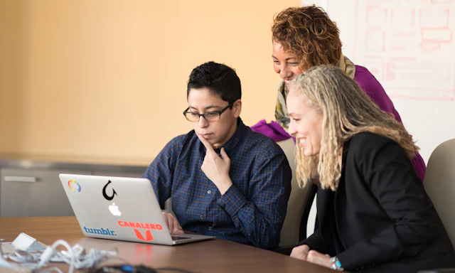 Group of coworkers crowded around a laptop on a table.